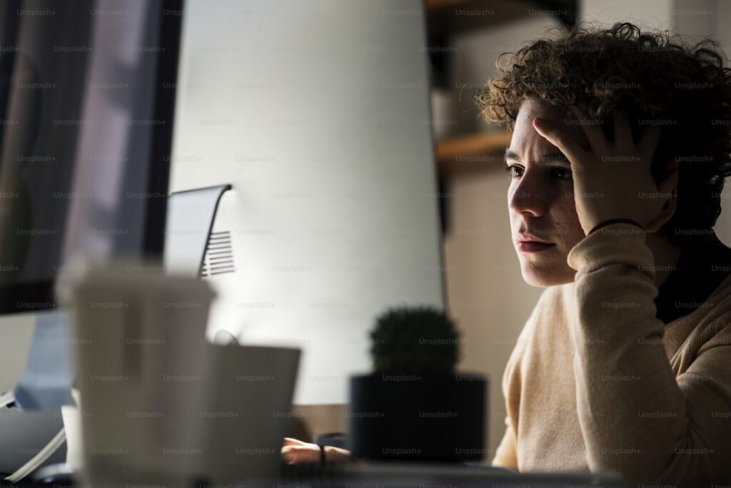 FXの借金や損失に不安を感じ、額に手を当てて悩んでいる大学生の男性。